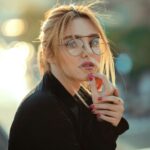 Portrait of a stylish woman wearing glasses, embracing natural light outdoors.