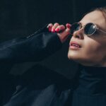 Elegant woman in sunglasses looking upwards under sunlight. Fashionable attire with modern style.