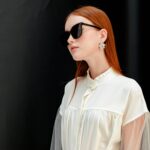 Fashion portrait of a stylish woman in sunglasses with elegant earrings and a chic white outfit.
