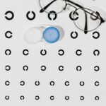 High angle view of eyeglasses and contact lens case on an eye test chart, emphasizing vision care.